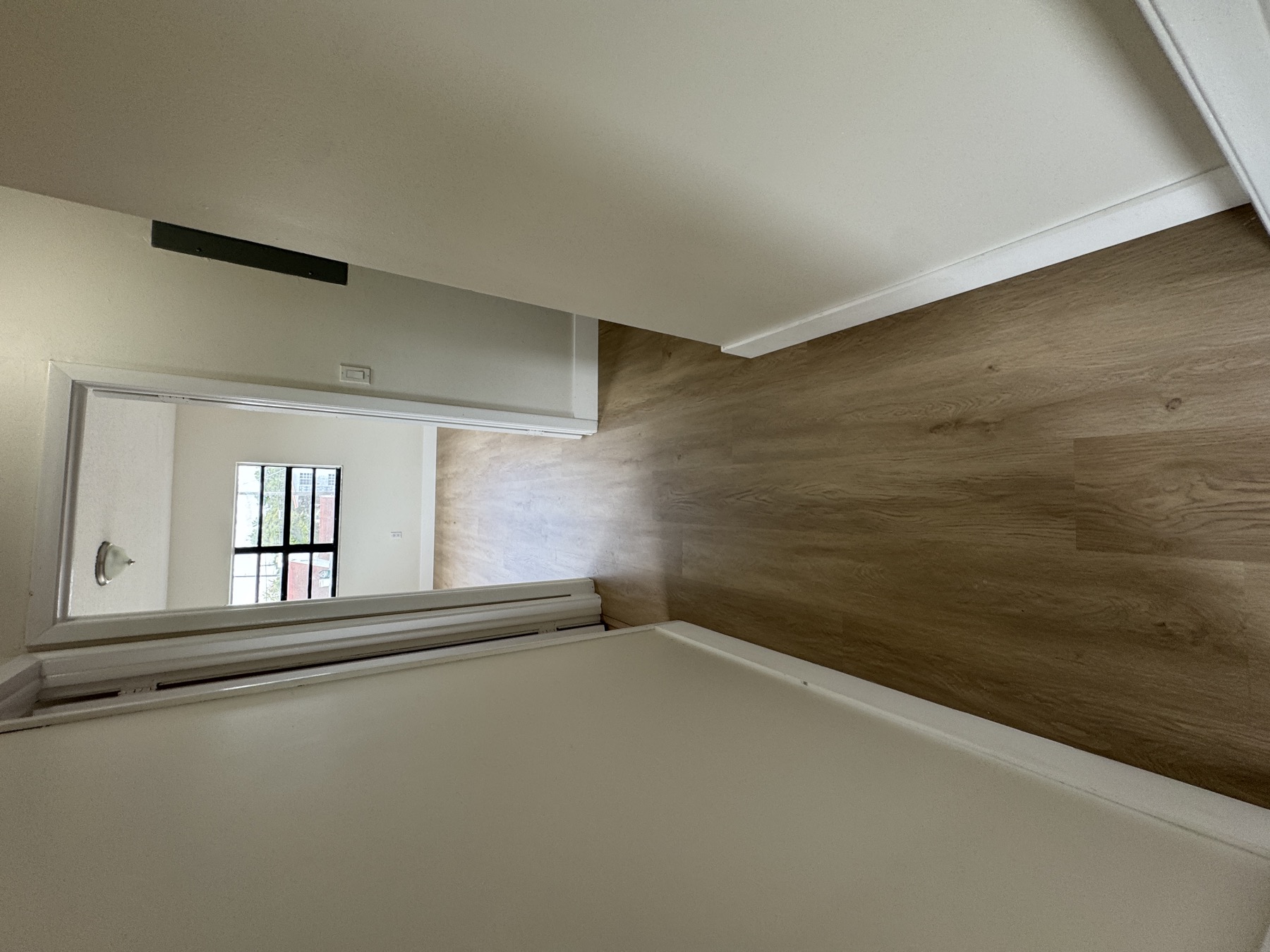 Hallway with continuous greige vinyl plank installed over tile, with new white baseboards