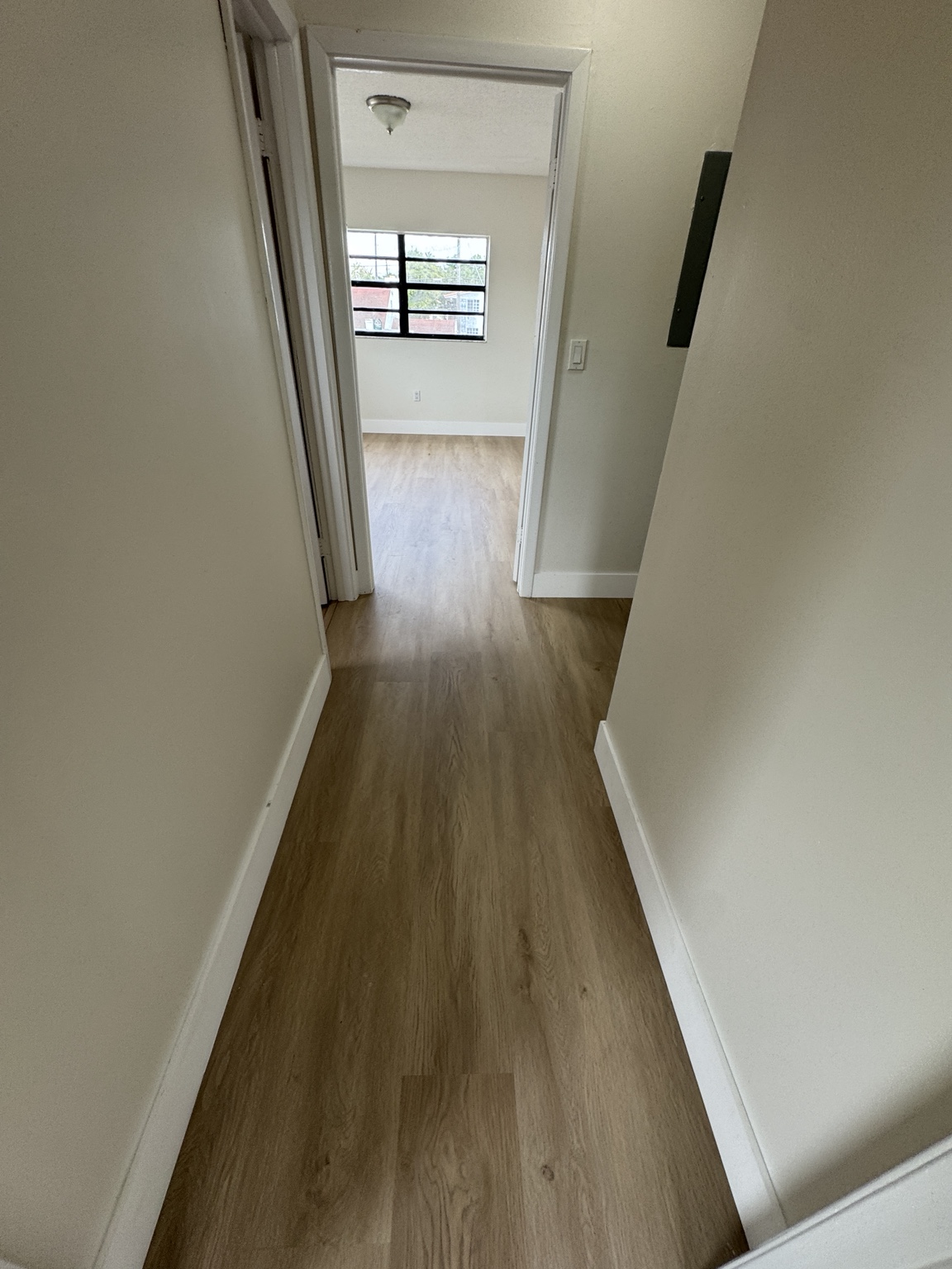 Hallway after installation with continuous light wood-look waterproof vinyl flooring and white baseboards.